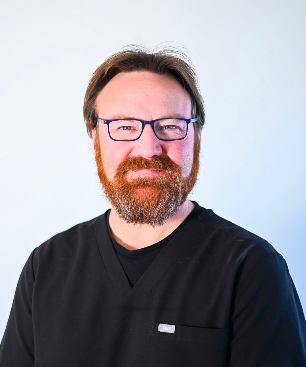 Bearded man in black scrubs, smiling portrait.