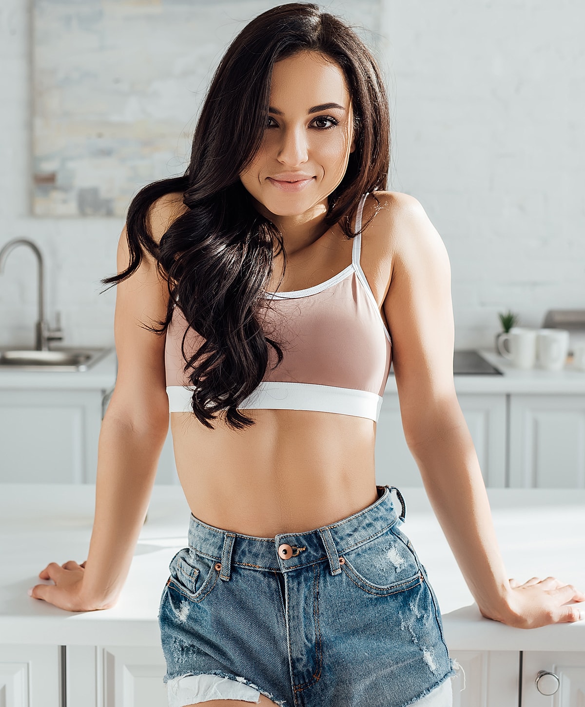 Woman smiling in casual attire at kitchen counter.